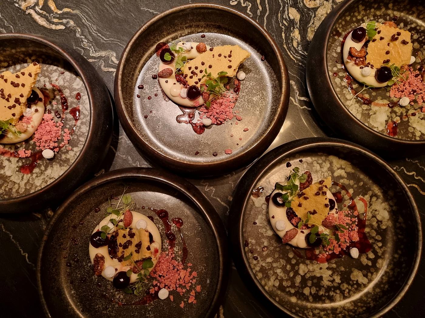 Vier opgemaakte desserts in donkere schalen op marmer